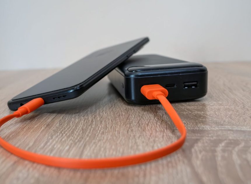 Павербанк з портами USB-C і USB-A заряджає смартфон помаранчевим кабелем
