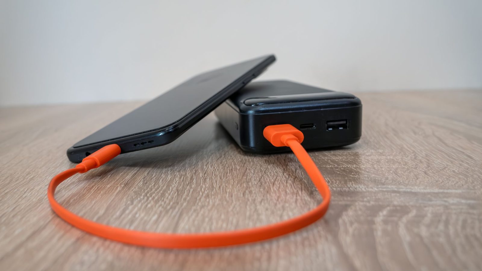 Павербанк з портами USB-C і USB-A заряджає смартфон помаранчевим кабелем