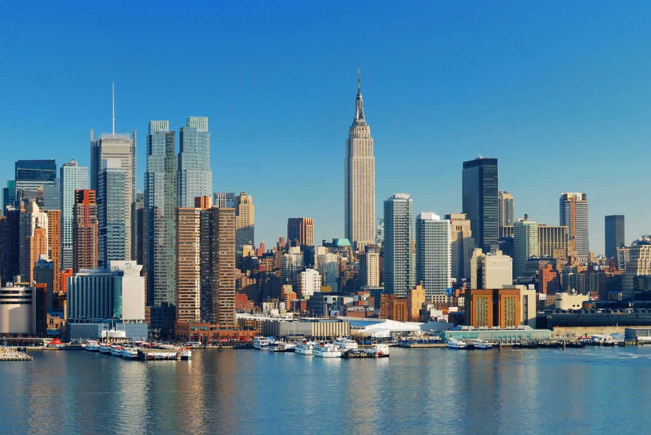New York City skyline with the Empire State Building rising above the harbor and boats along the waterfront