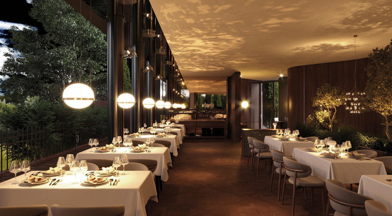 photo_2026-08-28_10-58-22 - TYME BLOG Evening fine-dining terrace with white-tablecloth tables, wine glasses, and warm pendant lights along a glass wall, surrounded by trees and greenery.