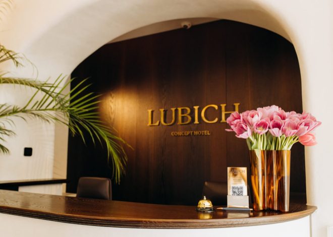 Reception desk at Lubich Concept Hotel with a dark wood backdrop and a gold sign, plus a copper vase of pink tulips on the counter