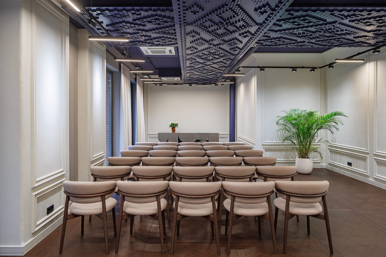 photo_2026-08-28_10-59-35 - TYME BLOG Rows of beige chairs facing a podium with a vase of flowers in a modern conference room.