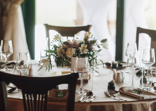 Table set for a formal event with wine glasses, cutlery, and a white-flower centerpiece across the table.