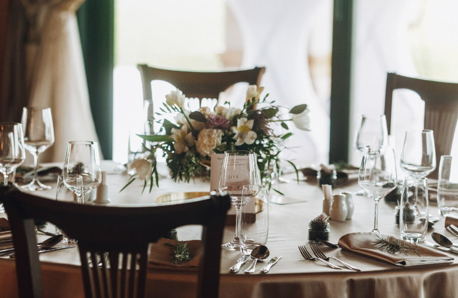 Table set for a formal event with wine glasses, cutlery, and a white-flower centerpiece across the table.