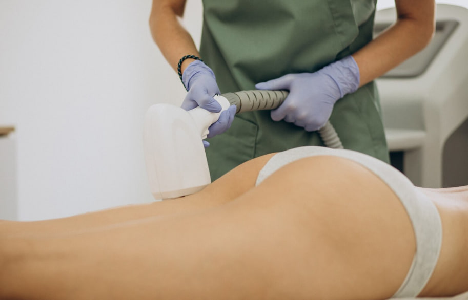 Gloved clinician performing a non-invasive body contouring treatment on a person lying face down over their buttocks with a handheld applicator.