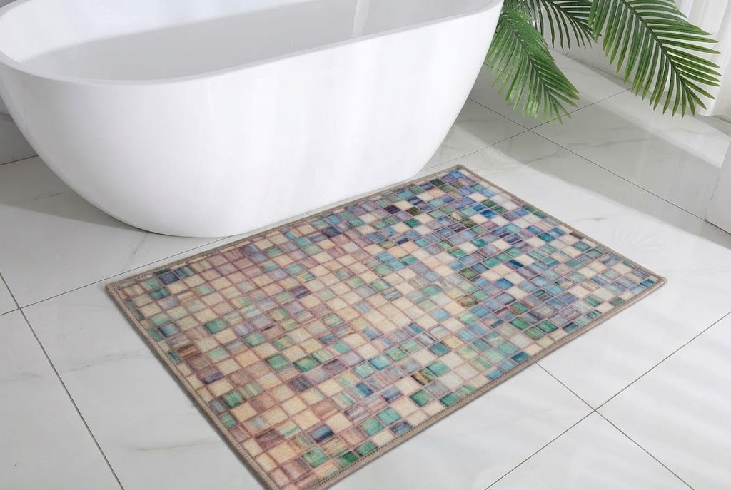 Multicolored mosaic rug on a white tiled bathroom floor beside a white freestanding tub and green plant leaves nearby.