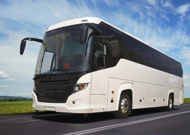 White passenger coach bus driving on an open road under a blue sky.