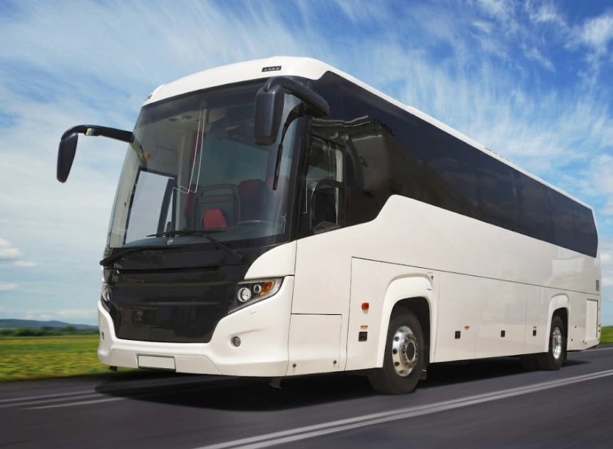 White passenger coach bus driving on an open road under a blue sky.