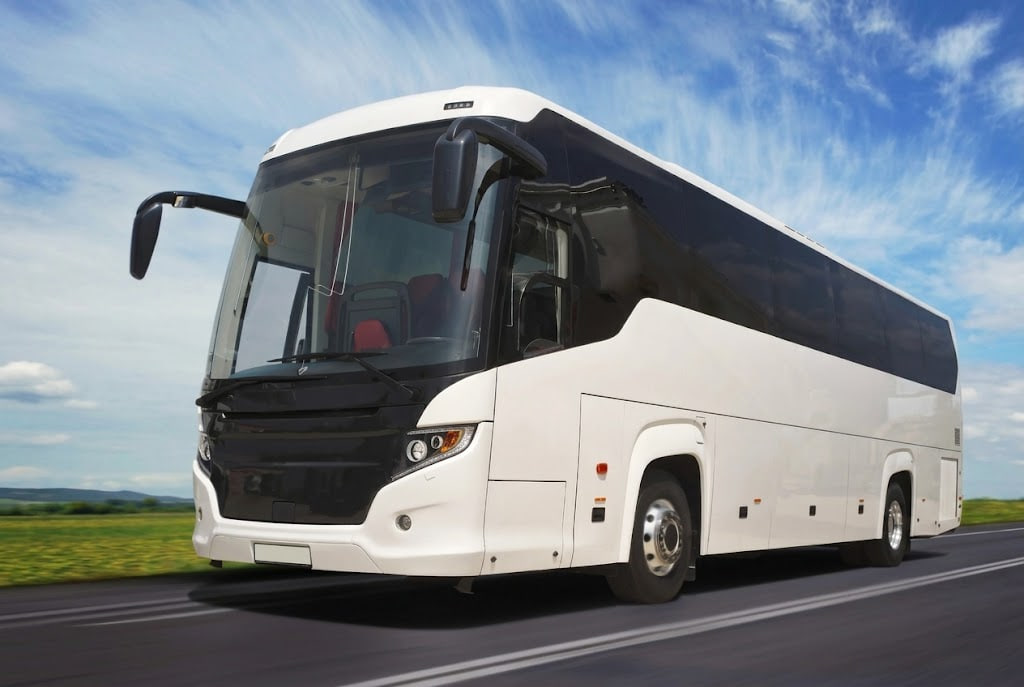 White passenger coach bus driving on an open road under a blue sky.