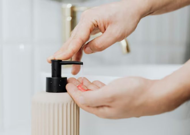 Hands pressing the pump of a beige soap bottle to dispense liquid soap into the other hand.