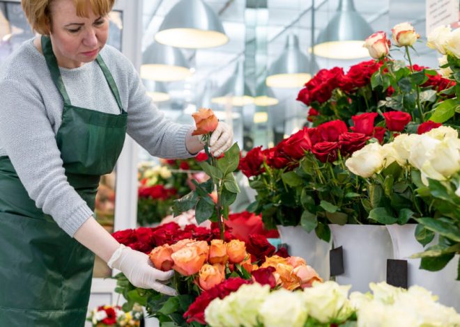 Florist in a green apron arranging orange and red roses in a bright shop