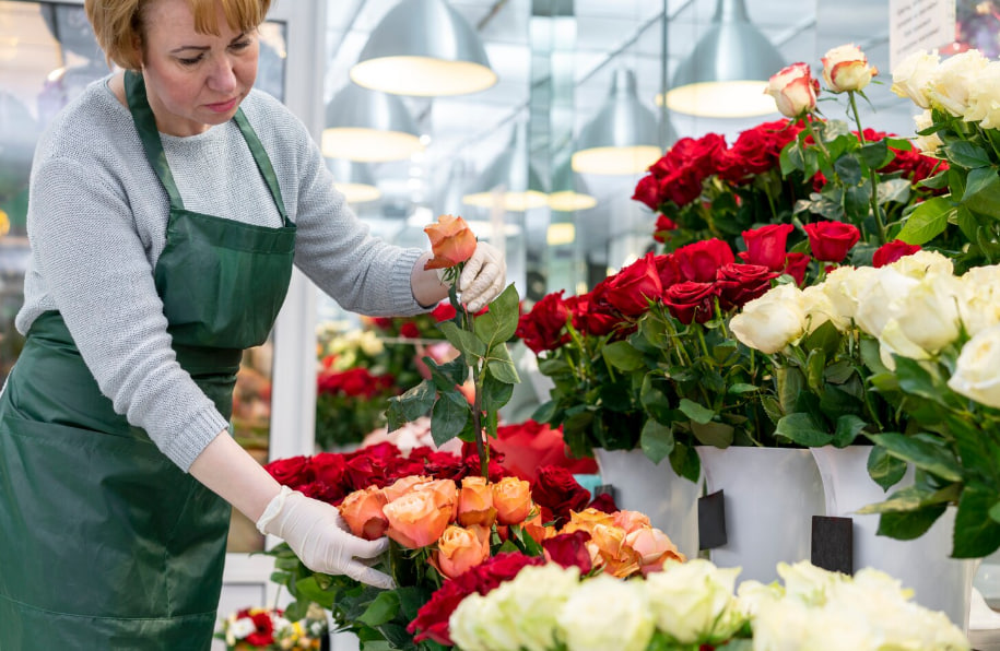 Florist in a green apron arranging orange and red roses in a bright shop