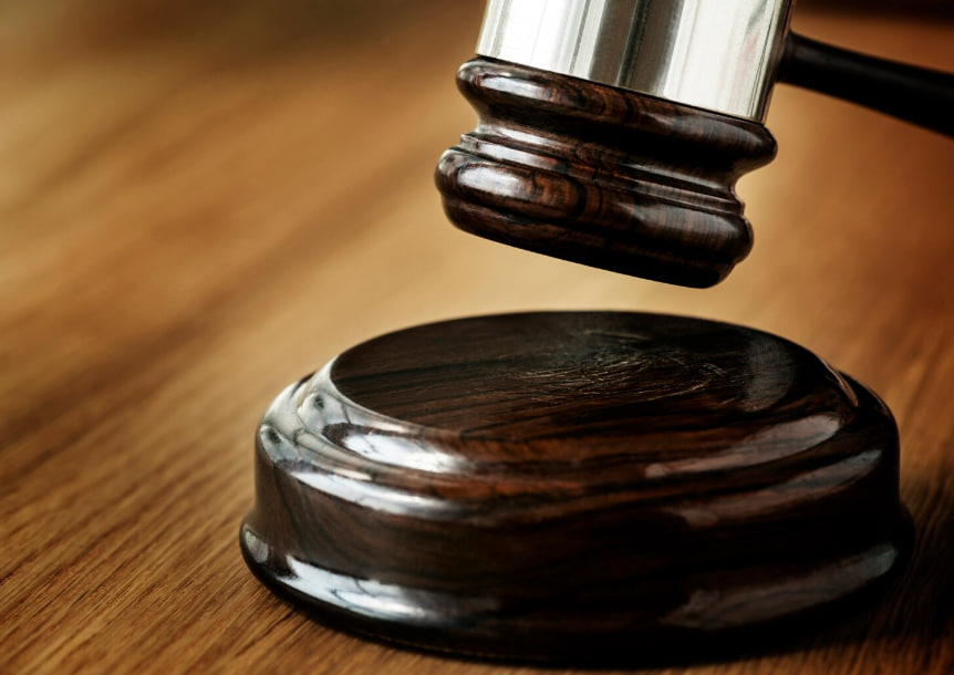 Close-up of a wooden judge's gavel about to strike a round sound block on a wooden table in a courtroom-style setting