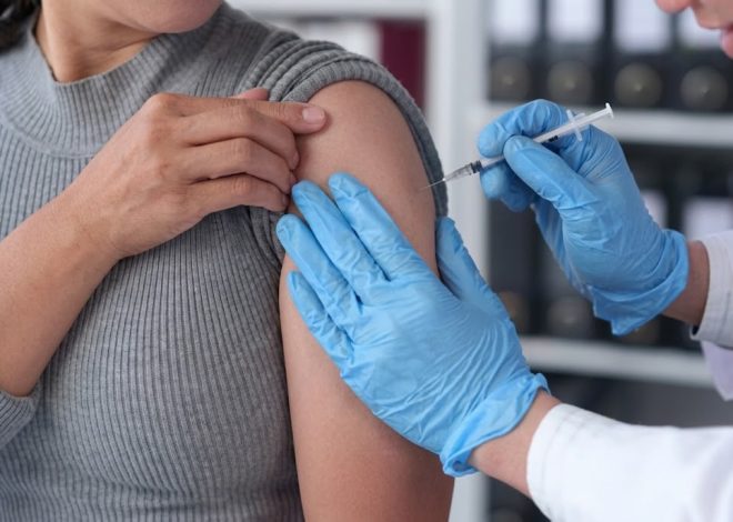 Healthcare professional in blue gloves administers a vaccine into a patient’s upper arm in a clinical setting.