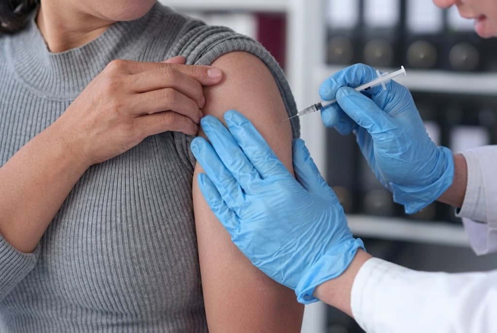 Healthcare professional in blue gloves administers a vaccine into a patient’s upper arm in a clinical setting.