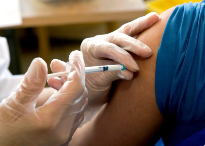 Nurse wearing gloves administers a syringe into a patient's upper arm during vaccination.