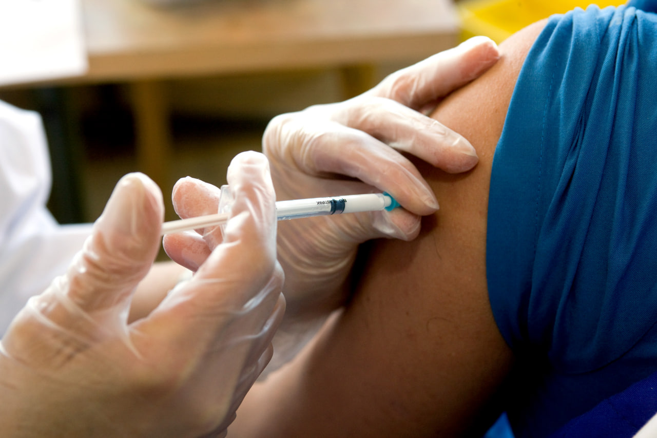 Nurse wearing gloves administers a syringe into a patient's upper arm during vaccination.