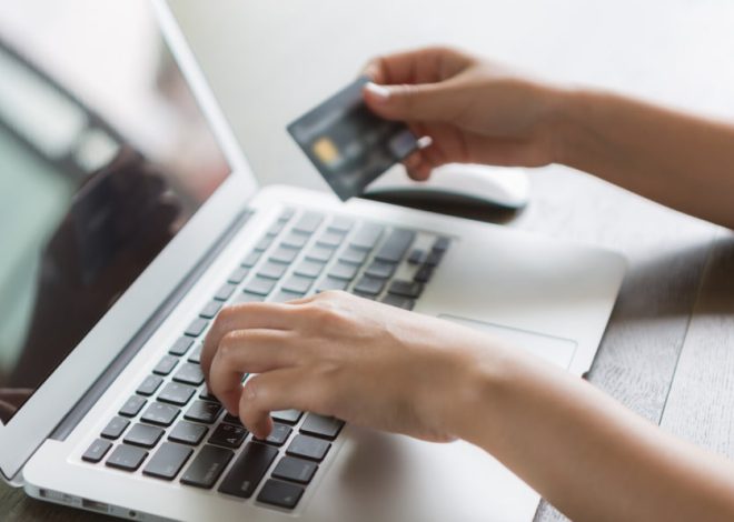 Person typing on a laptop while holding a credit card for online checkout.