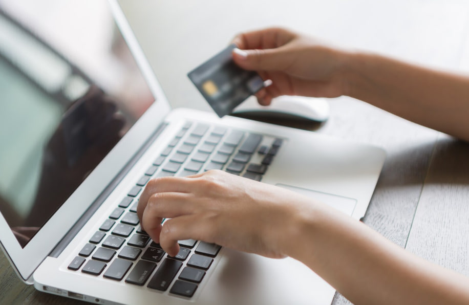 Person typing on a laptop while holding a credit card for online checkout.