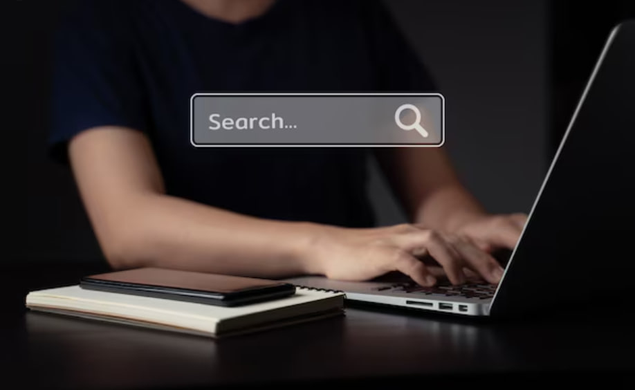 Person typing on a laptop at a dark desk; a translucent search box reading 'Search...' floats above.