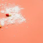 Assorted capsules and white powder spilled on a peach background, suggesting drug abuse.