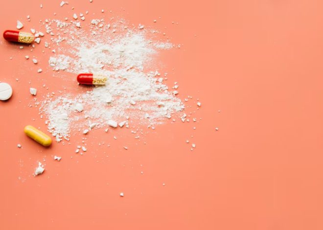 Assorted capsules and white powder spilled on a peach background, suggesting drug abuse.
