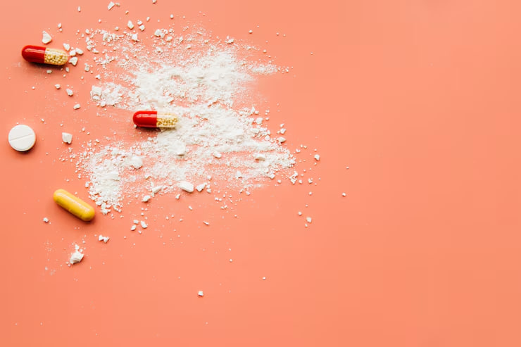 Assorted capsules and white powder spilled on a peach background, suggesting drug abuse.