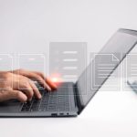 Hands typing on a laptop keyboard with translucent document icons floating above the device, suggesting digital files