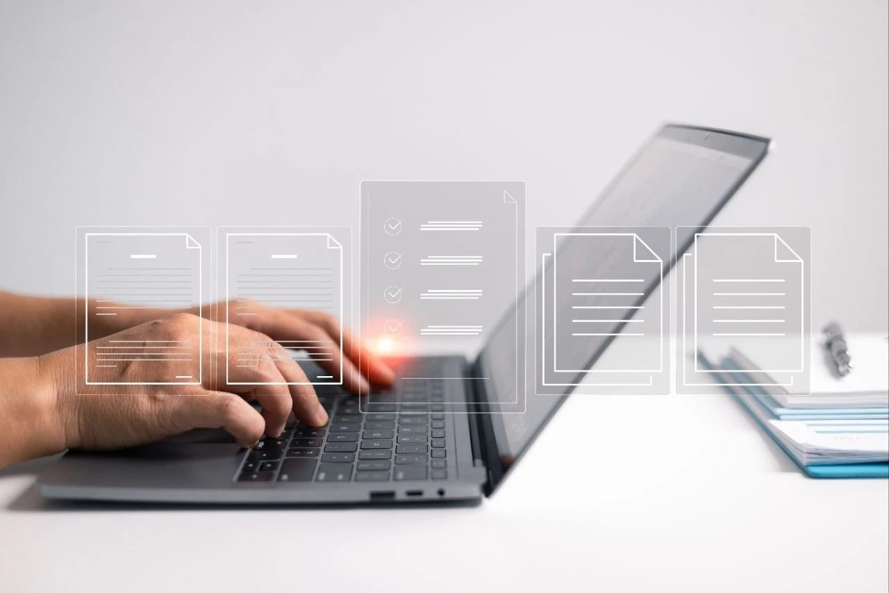 Hands typing on a laptop keyboard with translucent document icons floating above the device, suggesting digital files