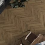 Overhead view of a herringbone wood floor with a small dining table and brown chairs, and potted plants in the corner.