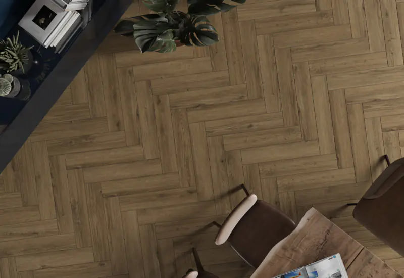 Overhead view of a herringbone wood floor with a small dining table and brown chairs, and potted plants in the corner.