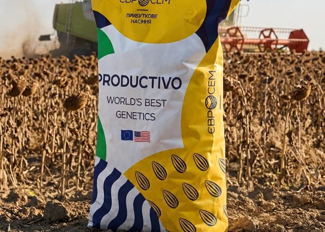 Colorful seed bag labeled 'PRODUCTIVO — World's Best Genetics' stands in a harvested field with a combine in the distance.