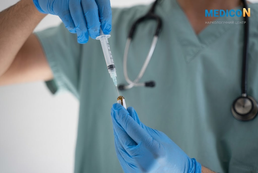Healthcare professional in blue gloves draws liquid from a vial with a syringe; stethoscope in view on scrubs.