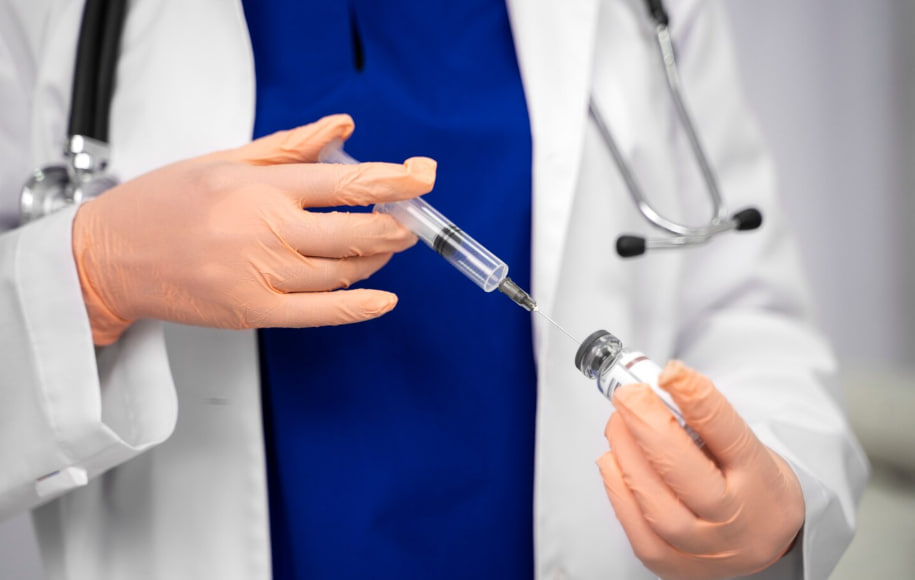 Doctor in gloves drawing vaccine from vial into a syringe in a clinical setting