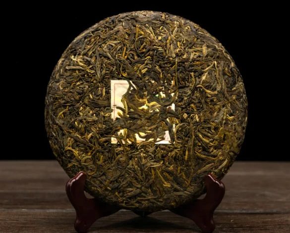 Round compressed tea cake made of dark leaves on a wooden stand against a black background.