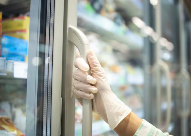 Gloved hand gripping a freezer door handle in a grocery store.