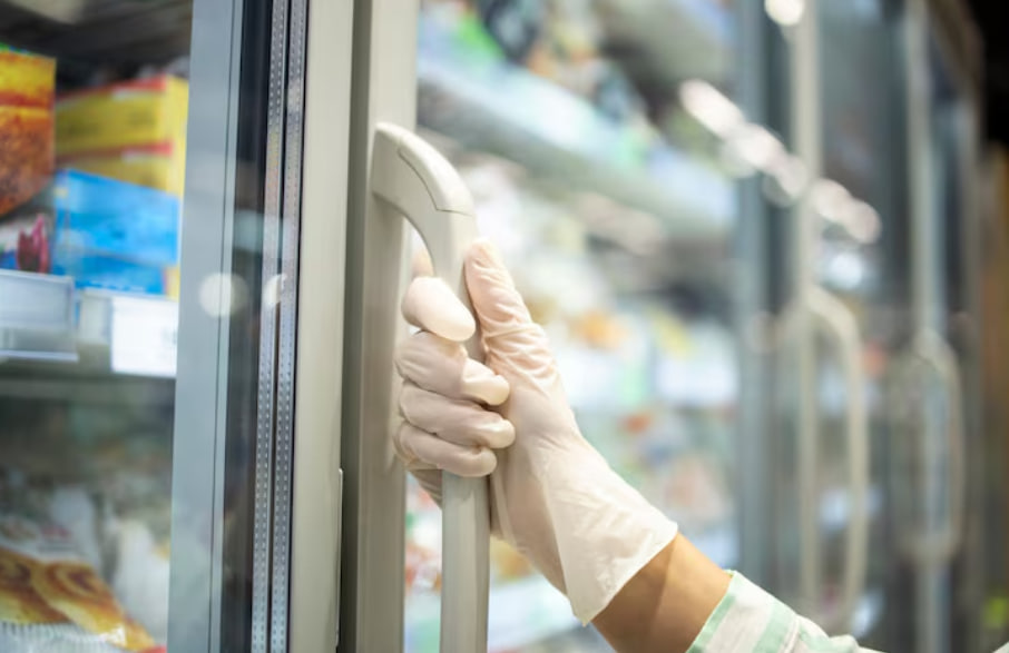 Gloved hand gripping a freezer door handle in a grocery store.