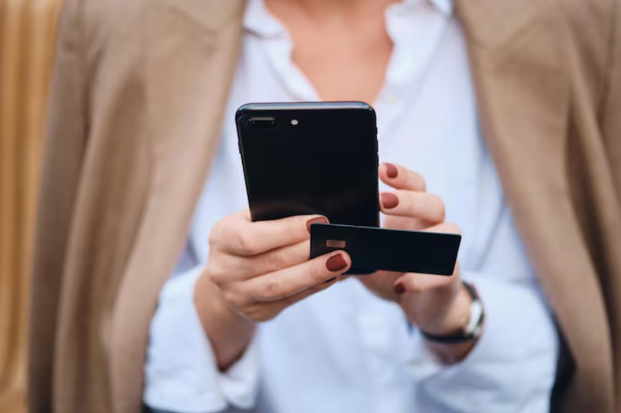 Person holding a smartphone and a credit card, ready to pay with a mobile wallet.