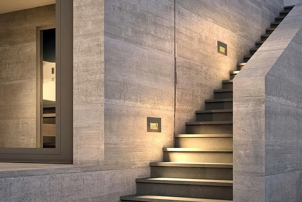 Modern interior concrete staircase with built-in square wall lights along a textured concrete wall
