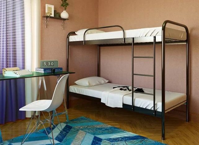Dorm room with a metal bunk bed, a glass desk, chair, and a blue geometric rug under wooden floor. Purple curtains frame a sunny window.