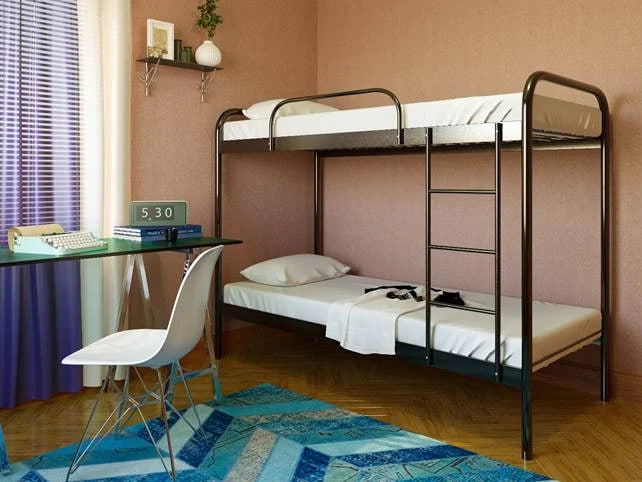 Dorm room with a metal bunk bed, a glass desk, chair, and a blue geometric rug under wooden floor. Purple curtains frame a sunny window.