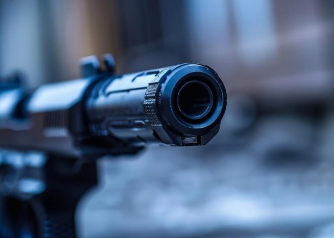 Close-up of a black pistol barrel aimed toward the camera with a blue-toned background.