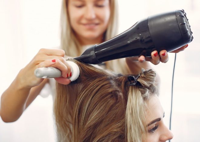 Hair stylist blow-drying a client’s hair with a black dryer in a salon setting.