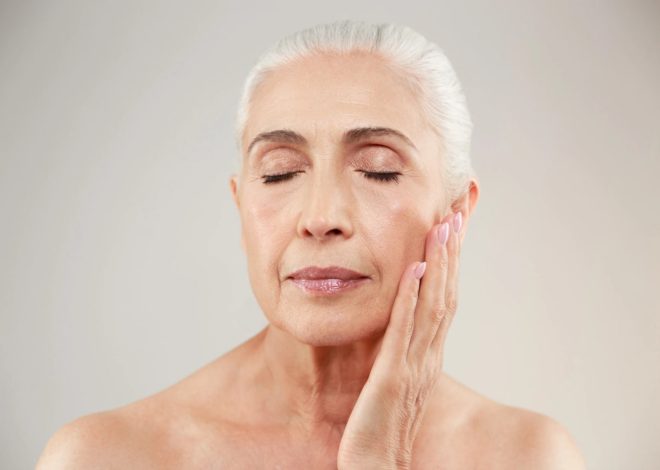Older woman with white hair, eyes closed, touching her cheek in a facial massage.