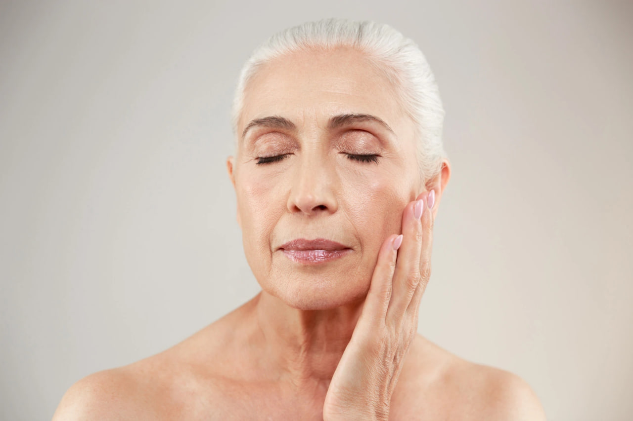 Older woman with white hair, eyes closed, touching her cheek in a facial massage.