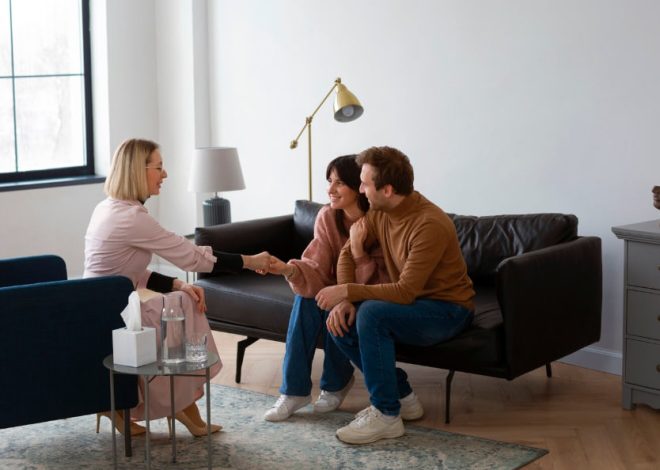 Therapist greets a smiling couple in a cozy living room as they shake hands, indicating a counseling session.