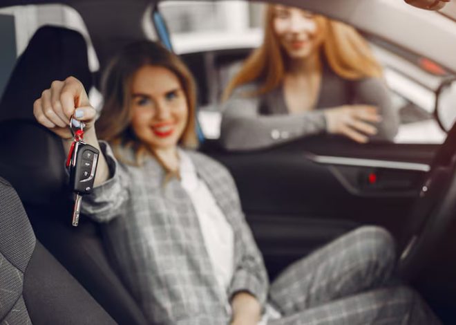 Woman in the driver's seat holds up car keys toward the camera as another woman smiles in the passenger seat behind her.