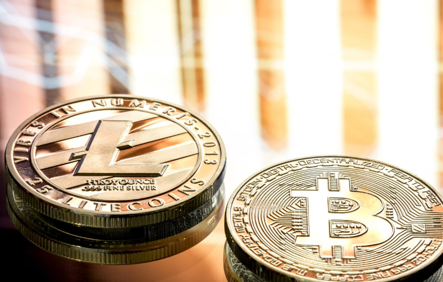 Close-up of Litecoin and Bitcoin coins stacked on a glossy surface with warm lighting, highlighting crypto symbols.