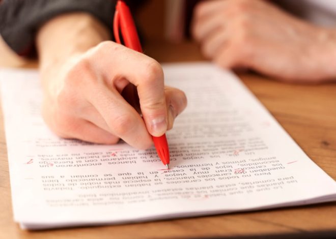 Person writing with a red pen on a printed document on a wooden table