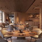 Elegant dining room with round wooden tables, gray upholstered chairs, and floral centerpieces in warm lighting